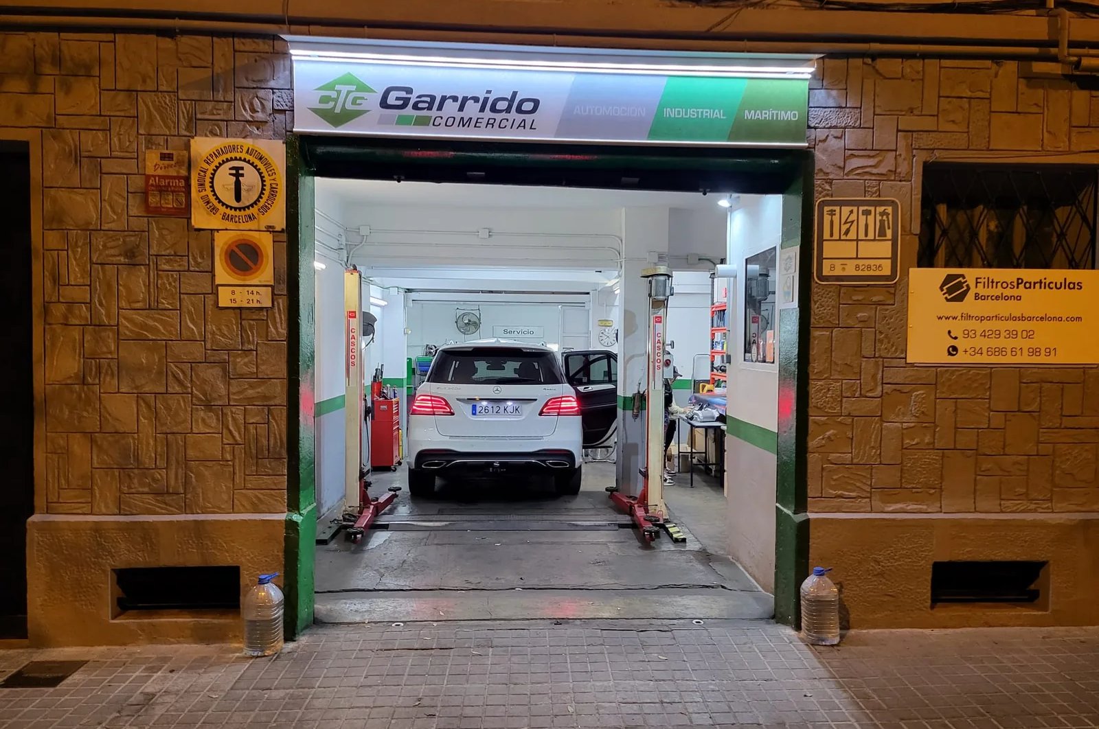 Entrada del taller de Filtro Partículas Barcelona en Nou Barris, de noche, con un vehículo en el elevador